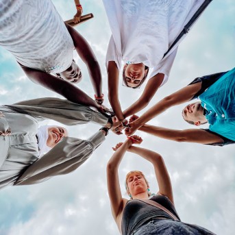 Five people standing in a circle around the camera that&#039;s laying on the ground facing the sky, whilst crossing their arms together in the centre.